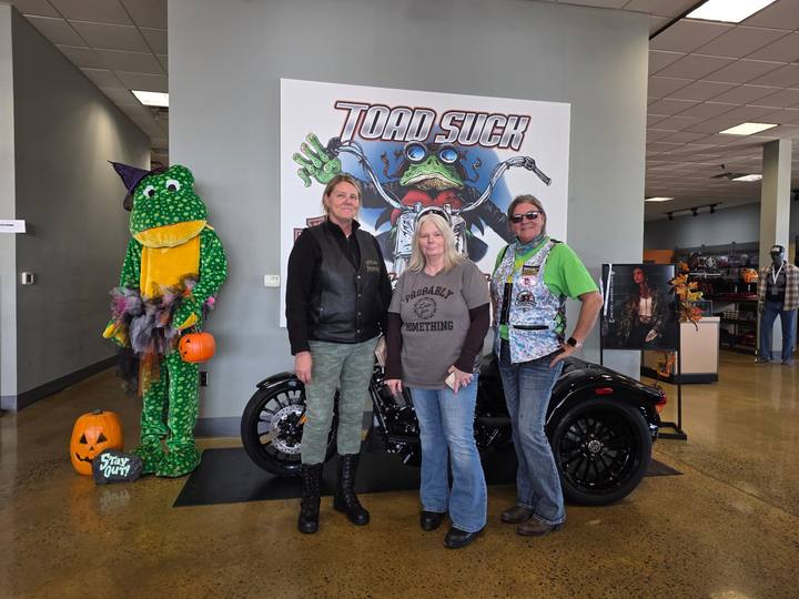 Three members beside a frog mascot in front of a Toad Suck sign