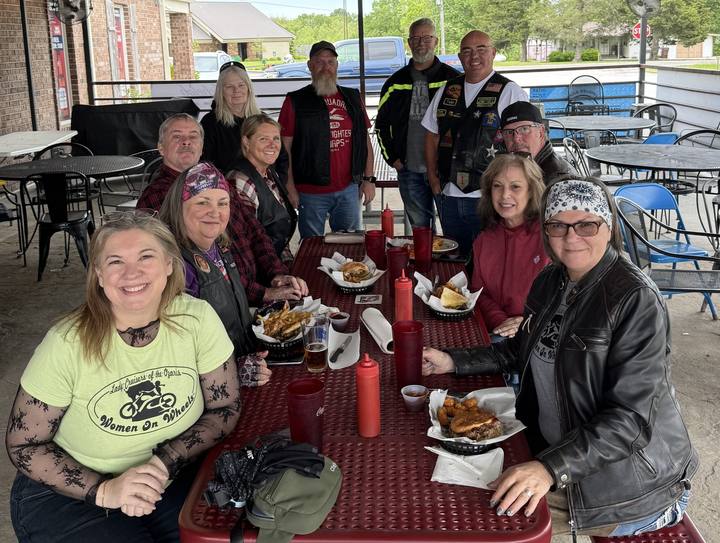 Riders sharing lunch at a long table on a restaurant patio