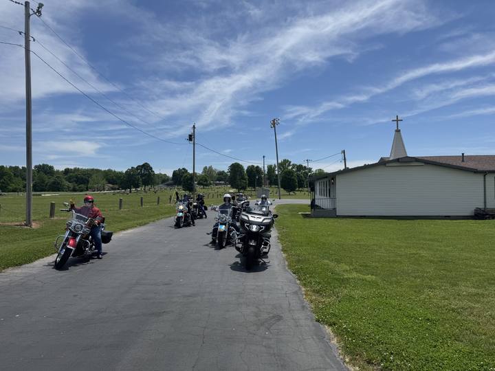 Two motorcycles on a road leading to a white church steeple