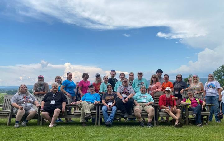 A large group seated and standing on a lawn under a wide blue sky