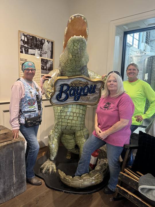 Two members smiling beside a large alligator statue and a Bayou sign
