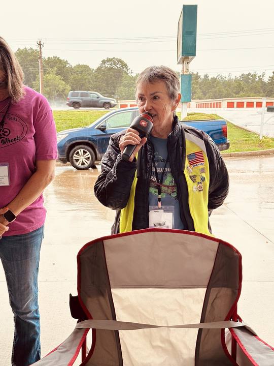 A rider in a safety vest speaking into a microphone at the Blessing of the Bikes