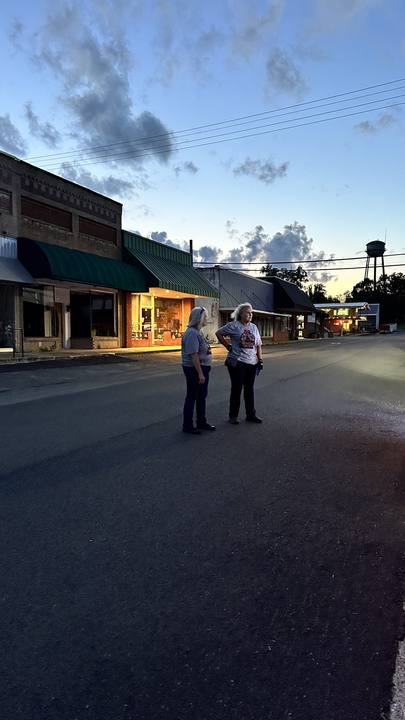 Two riders standing on a small-town main street at dusk