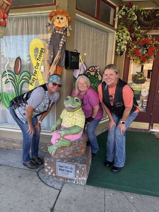 Three members posing with a frog statue