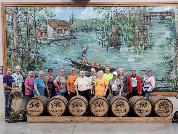 A group posed in front of a bayou mural and wooden barrels